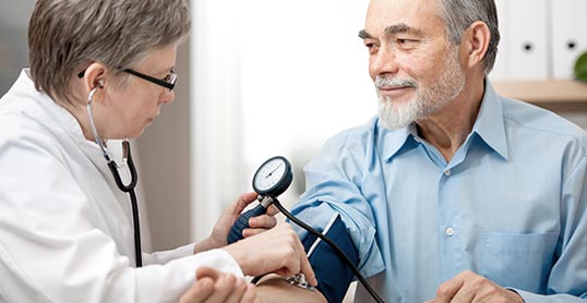 A woman checking the blood pressure of an older man.
