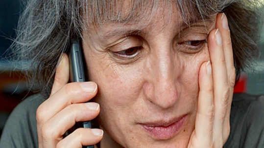A woman holding her head while talking on the phone.