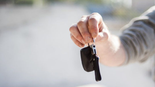 A person holding up a car key in their hand.